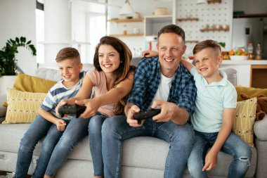 Karı koca oturma odasında joysticklerle oyun oynuyorlar. Sevgili çift evde çocuklarla video oyunu oynuyor..