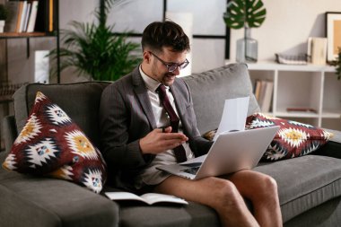 Evde pantolonsuz çalışan bir iş adamı. Genç adam video görüşmesi sırasında bilgisayarı kullanıyor..