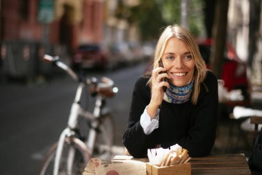 Kafede telefonla konuşan ve bilgisayarla çalışan genç ve güzel bir kadın..