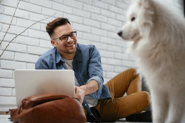 Adam dizüstü bilgisayarla çalışırken köpeğiyle yerde oynuyor. Samoe köpeğiyle oynayan adam..