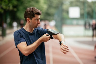 Genç adam antrenman sırasında kalp atışlarını kontrol ediyor. Genç adam atletizm pistinde egzersiz yapıyor..