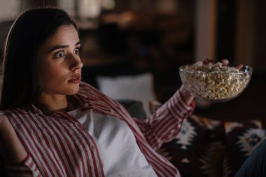 Gece film izleyen güzel bir kadın evdeki oturma odasında bir kanepede oturuyor.