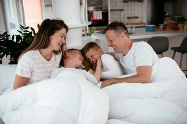 Genç bir aile yatakta eğleniyor. Oğulları yatakta dinlenen mutlu ebeveynler.