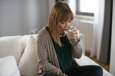 Genç hasta kadın ilaç alıyor. Kanepede oturan güzel bir kadın karın ağrısı çekiyor..