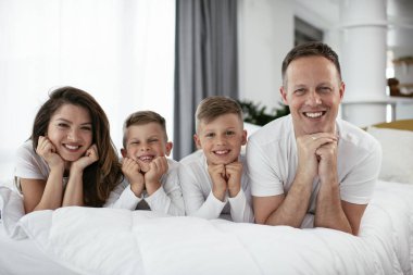 Genç bir aile yatakta eğleniyor. Oğulları yatakta dinlenen mutlu ebeveynler.