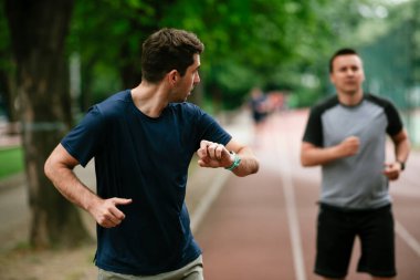 Gençler yarış pistinde antrenman yapıyor. İki genç arkadaş atletizm pistinde koşuyor.