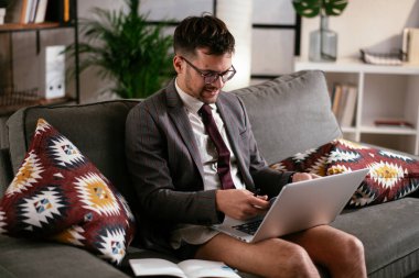 Evde pantolonsuz çalışan bir iş adamı. Genç adam video görüşmesi sırasında bilgisayarı kullanıyor..