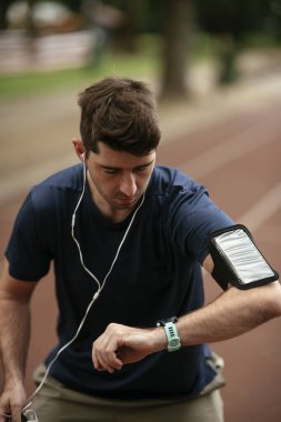 Genç adam antrenman sırasında kalp atışlarını kontrol ediyor. Genç adam atletizm pistinde egzersiz yapıyor..