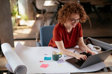 Güzel bir iş kadını proje üzerinde çalışıyor. Ofiste kıvırcık saçlı genç bir kadın var..