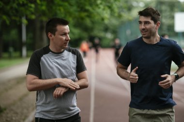 Gençler yarış pistinde antrenman yapıyor. İki genç arkadaş atletizm pistinde koşuyor.