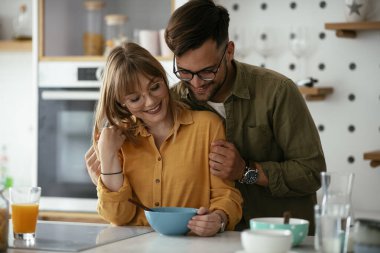 Genç çift evde kahvaltı hazırlıyor. Sevgi dolu çift mutfakta mısır gevreği yiyor..