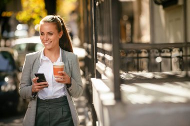 Kahve fren yaparken sokakta telefon kullanan genç ve mutlu bir iş kadını.