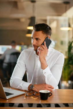 İş adamı telefonda iş konuşuyor. Genç işadamı ofiste telefonda konuşuyor..