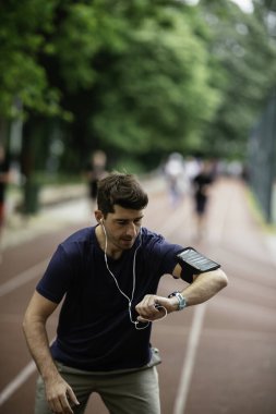 Genç adam antrenman sırasında kalp atışlarını kontrol ediyor. Genç adam atletizm pistinde egzersiz yapıyor..