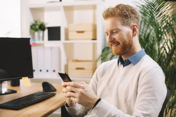 handsome businessman with ginger hair using smartphone in the office