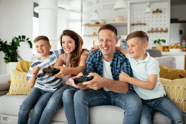 Husband and wife playing video games with joysticks in living room. Loving couple  playing video games with kids at home.