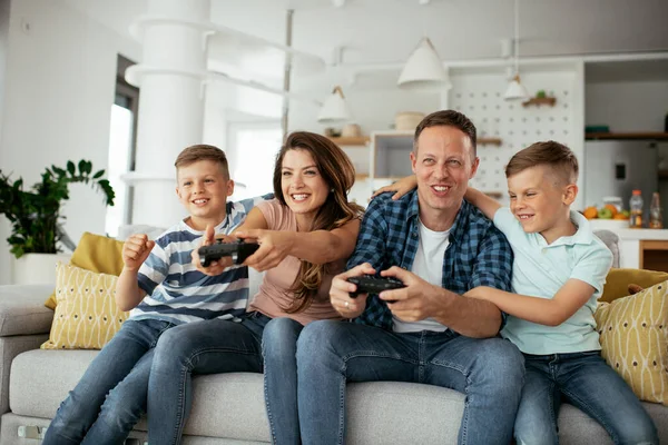 Husband and wife playing video games with joysticks in living room. Loving couple playing video games with kids at home.