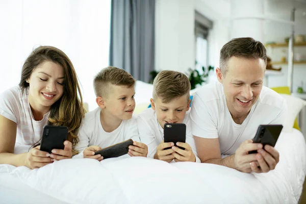 Family using mobile phones. Parents and kids using smart phones at home.