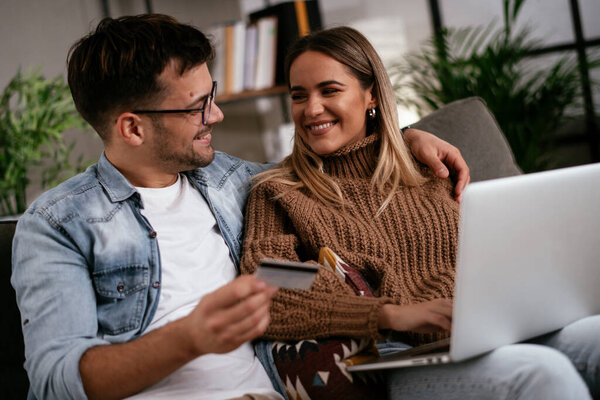 Young couple using credit card and laptop at home. Boyfriend and girlfriend buying online.