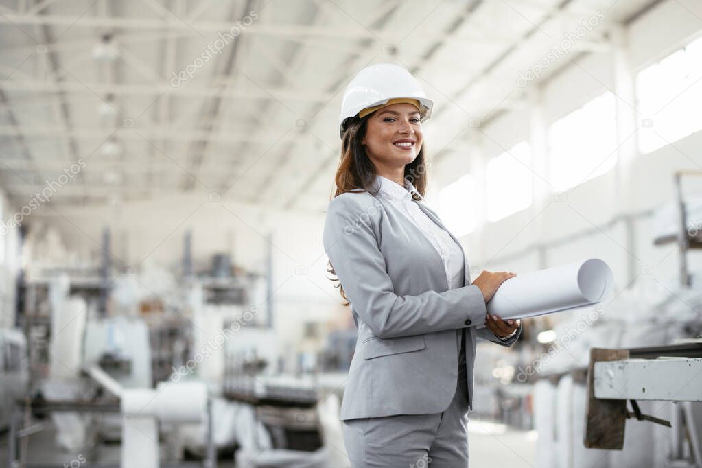 portrait of beautiful architect woman with blueprint standing in a factory