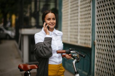 Akıllı telefon kullanan bisikletli genç bir kadın.