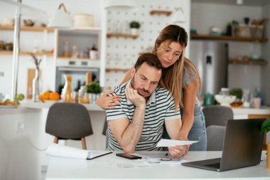 Yorgun çift mutfaktaki masada belgeleri inceliyor.