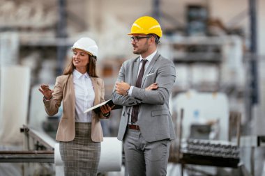 İşadamı ve iş kadını fabrikada iş konuşuyorlar.