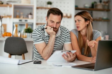 Yorgun çift mutfaktaki masada belgeleri inceliyor.