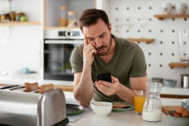 Genç adam kahvaltı yapıyor ve internette haberleri okuyor..