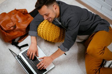 Yakışıklı genç adam evde yerde yatarken dizüstü bilgisayarda çalışıyor.