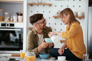 Genç çift evde kahvaltı hazırlıyor. Sevgi dolu çift mutfakta mısır gevreği yiyor..