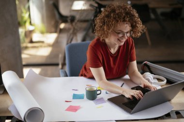 Güzel bir iş kadını proje üzerinde çalışıyor. Ofiste kıvırcık saçlı genç bir kadın var..