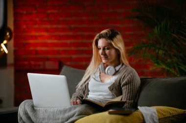 Güzel bir genç kadın evinde dizüstü bilgisayar çalışıyor ve çalışıyor..