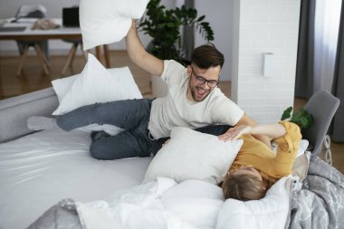 Erkek arkadaş ve kız arkadaş yatakta yastık kavgası yapıyor. Mutlu çift evde eğleniyor.