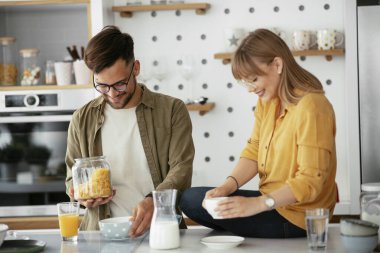 Genç çift evde kahvaltı hazırlıyor. Sevgi dolu çift mutfakta mısır gevreği yiyor..