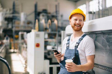 Sarı miğferli mutlu işçi fabrikada telefon kullanıyor. 