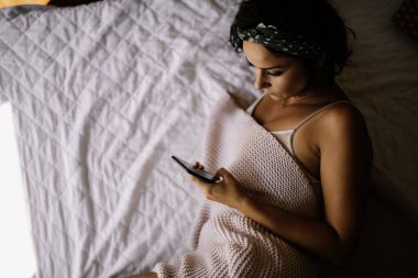 Yatakta telefon kullanan genç ve güzel bir kadın. Yatakta yatan kız..