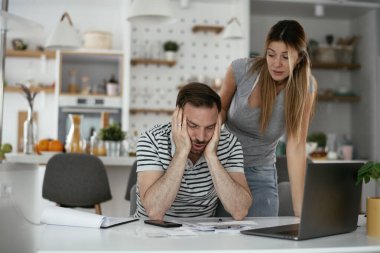 Yorgun çift mutfaktaki masada belgeleri inceliyor.