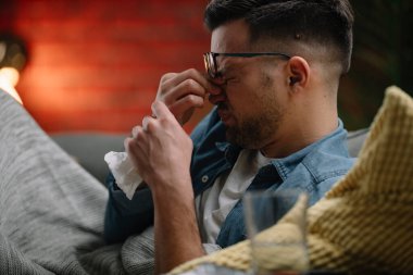 Genç adam evde hasta. Erkek, kanepede yatıyor ve ateşi var..