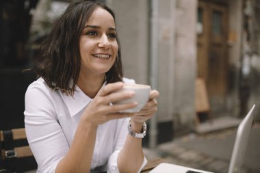 Güzel, genç, esmer iş kadını kahve içiyor ve sokak kafesinde çalışıyor.