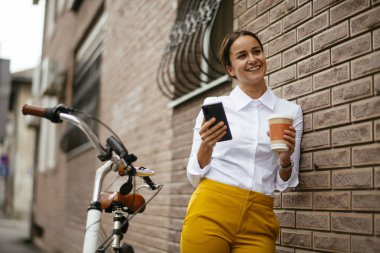 Akıllı telefon kullanan bisikletli genç bir kadın.