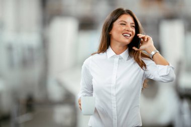 Genç iş kadını cep telefonuyla konuşuyor. Fabrikada proje yöneticisi.