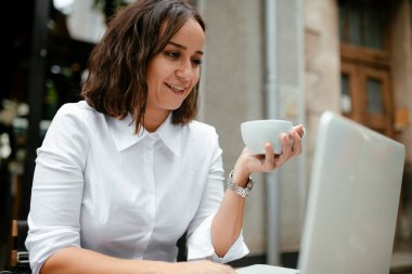 Güzel, genç, esmer iş kadını kahve içiyor ve sokak kafesinde çalışıyor.