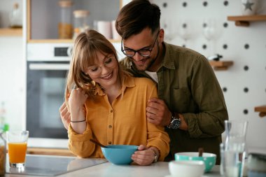 Genç çift evde kahvaltı hazırlıyor. Sevgi dolu çift mutfakta mısır gevreği yiyor..