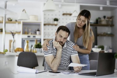 Yorgun çift mutfaktaki masada belgeleri inceliyor.