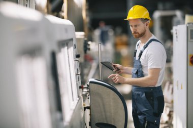 Üretim hattındaki fabrika işçisi. Fabrikada çalışan sarı kasklı adam..
