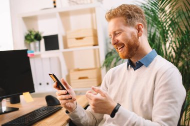 Ofiste akıllı telefon kullanan kızıl saçlı yakışıklı bir iş adamı.