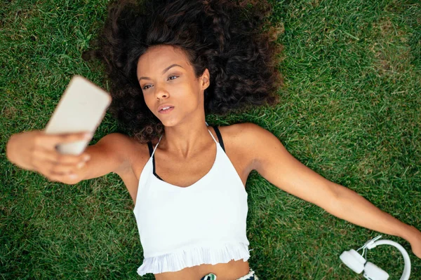 Güzel Afrikalı kız çimenlerde uzanıp selfie çekiyor.