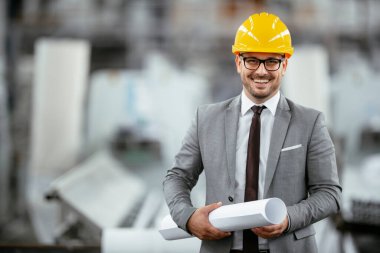 Fabrikada sarı kasklı gri takım elbiseli bir işadamının portresi..