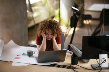 Yorgun ve güzel iş kadını proje üzerinde çalışıyor. Ofiste kıvırcık saçlı genç bir kadın var..